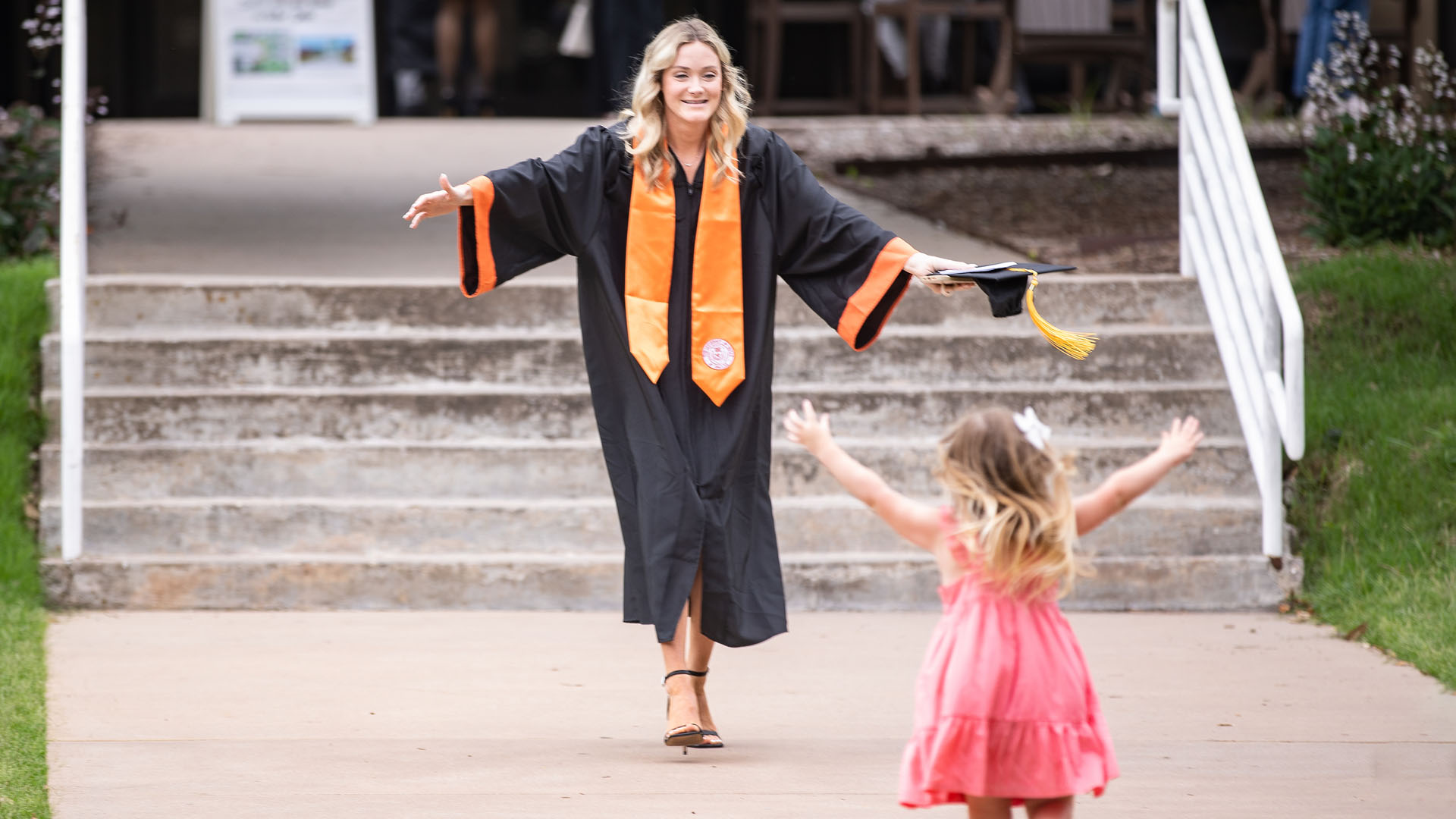 A graduate holds her arms out as a child runs toward her.