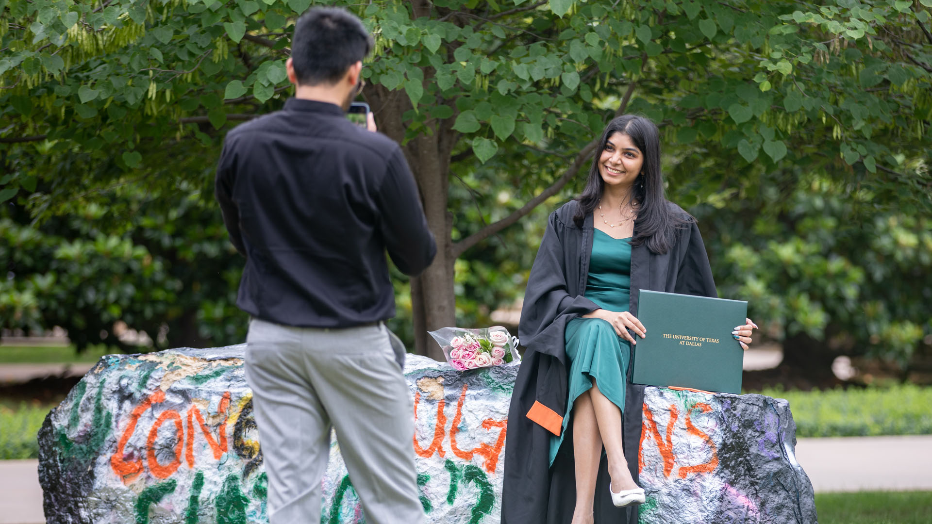 A person takes a photo of a graduate sitting on Spirit Rocks.